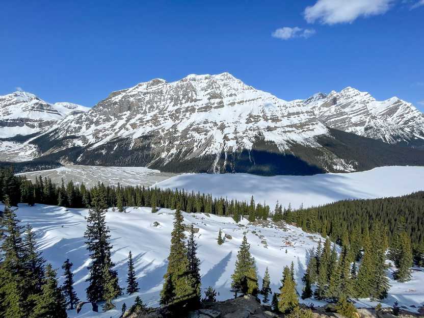 A view of a frozen and snow covered lake from above. Mountains covered in snow are on the opposite side of the lake.