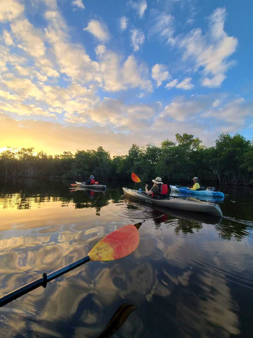Three people kayaking with the reflection of the sunrise onto the water.