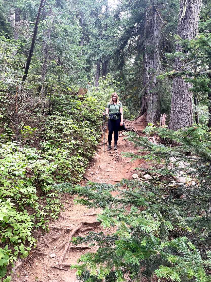 Lydia facing the camera up on a hill during a hike in Washington. She has a trekking poll and her jacket tied around her waist. Lydia facing the camera up on a hill during a hike in Washington. She has a trekking poll and her jacket tied around her waist.