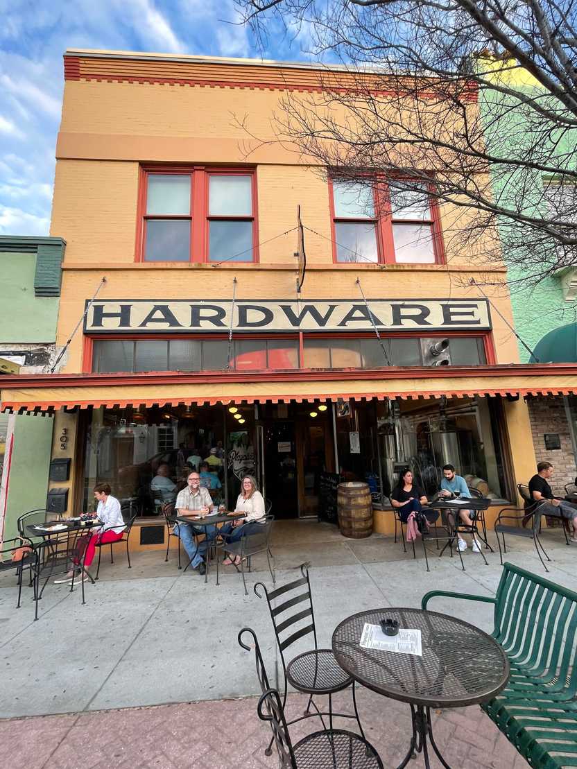 A yellow building labeled 'hardware' with tables out front. A yellow building labeled 'hardware' with tables out front.