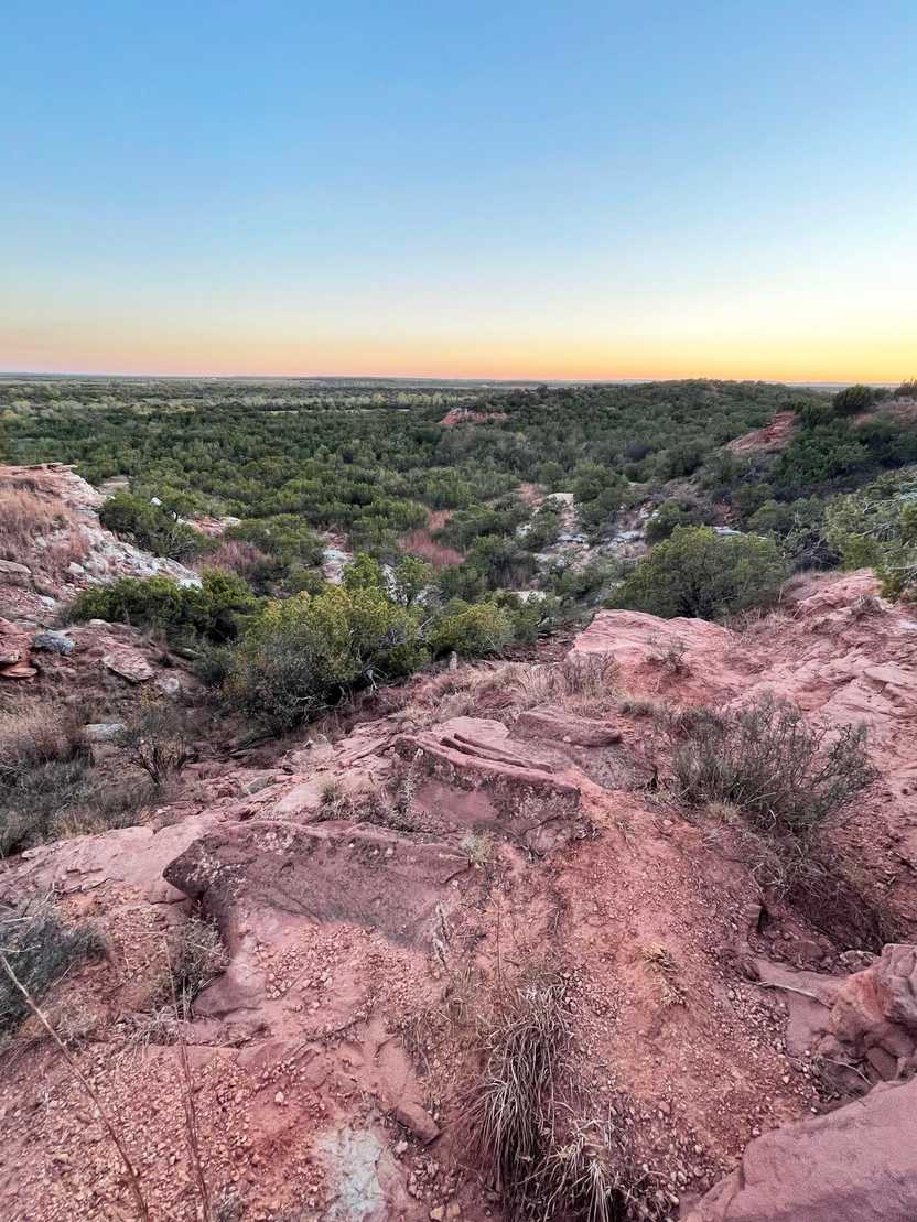 Pink rocks with trees in the distance at sunset in Copper Breaks State Park.