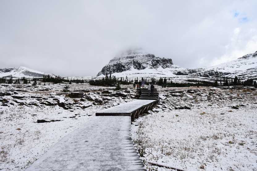 A snow covered boardwalk trail leading up to a mountain.