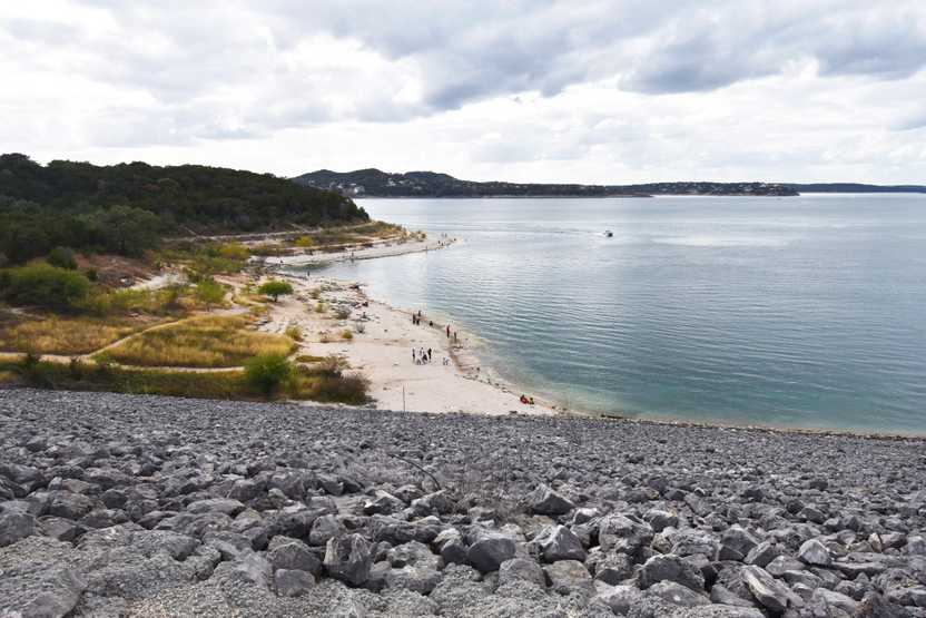 Looking down from a dam at Canyon Lake. A beach sits on the banks of the water.