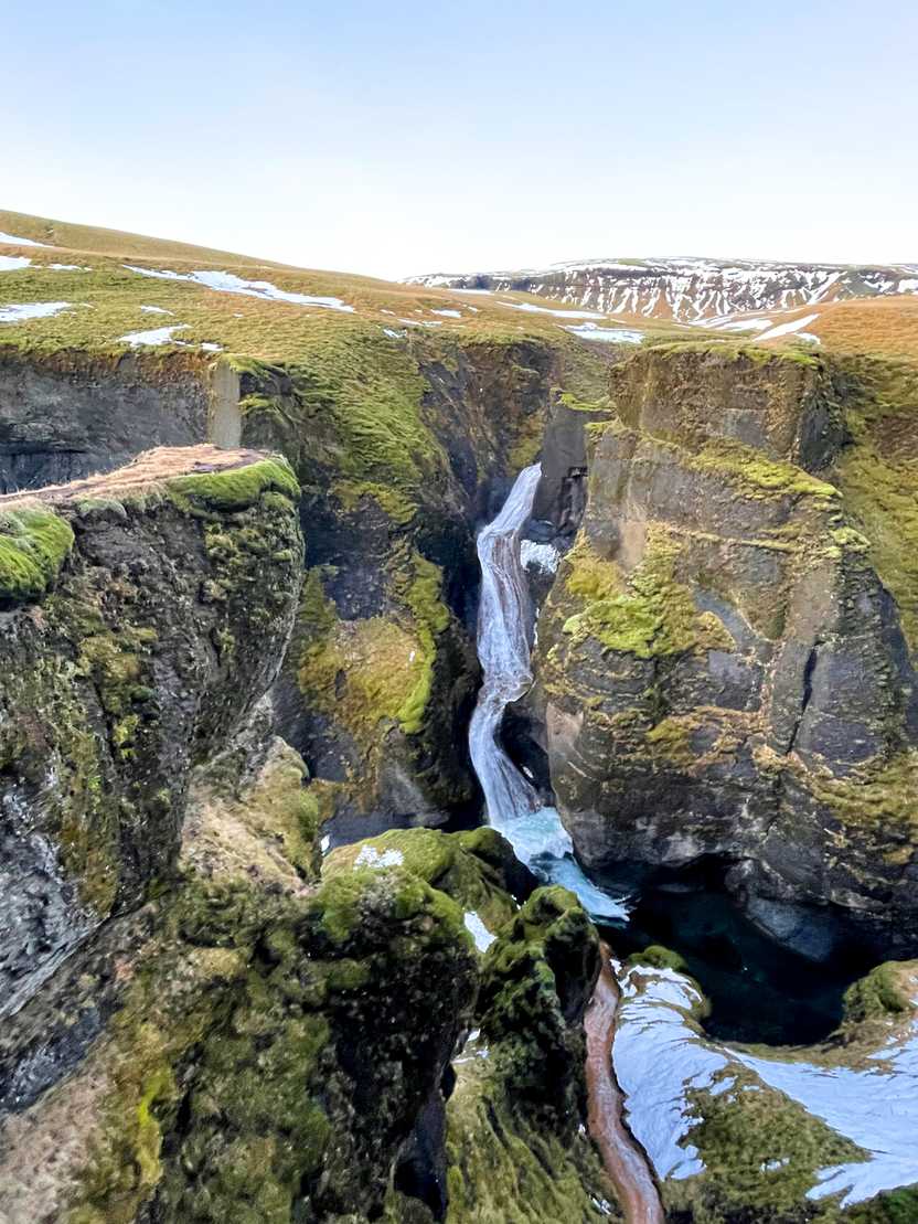 A waterfall cascading down a canyon. The canyon is covered in bright greenery