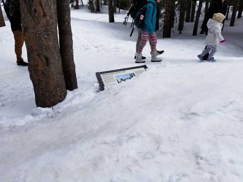 A sign on the trail that is almost completed buried in several feet of snow.