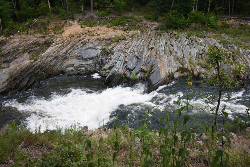 Looking down at the river along the Friends Loop trail. There are interesting rocks next to the water and greenery on both sides of the water.