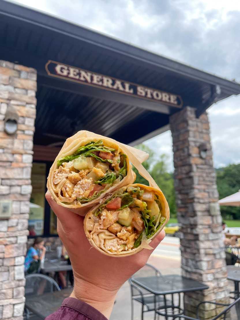 Holding up burrito cut in half from Falls Market. The burrito has greens, vegetables and tofu.