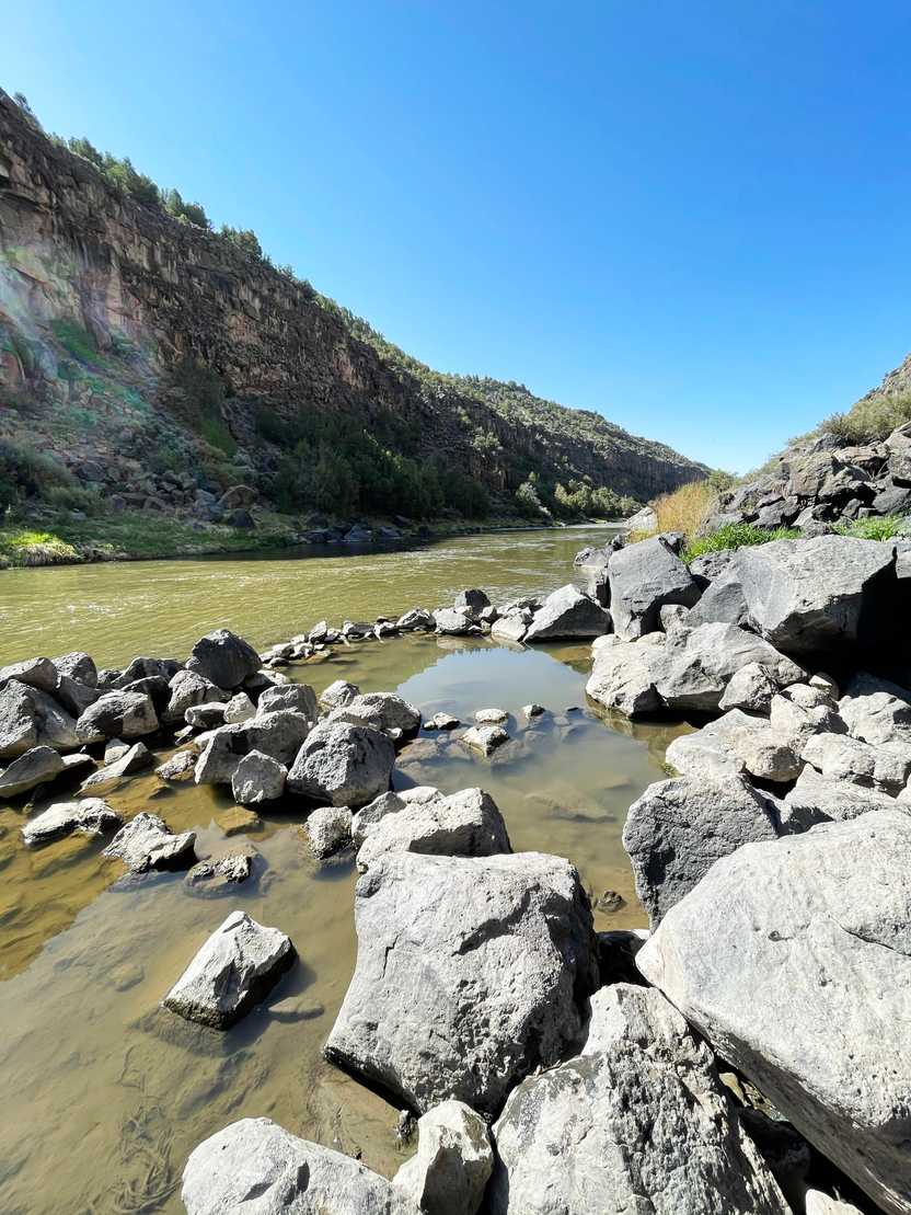 Several gray rocks next to a river. Some of the rocks create a round pool area.