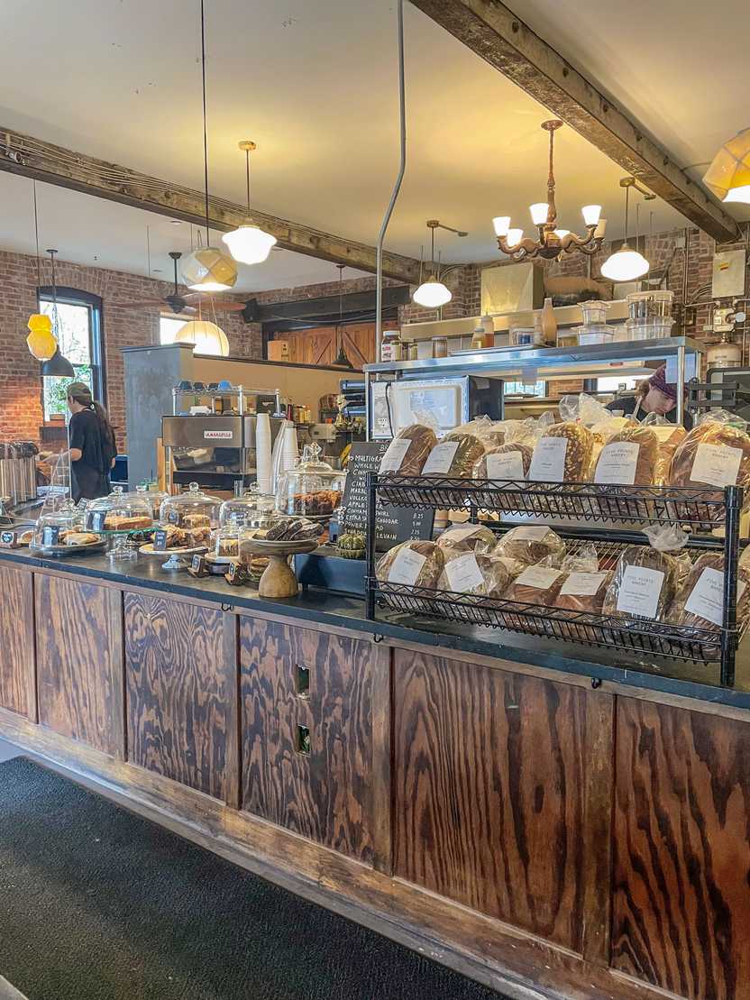 Bagged breads and pastries sitting on top of a wooden counter inside of Five Points Bakery.