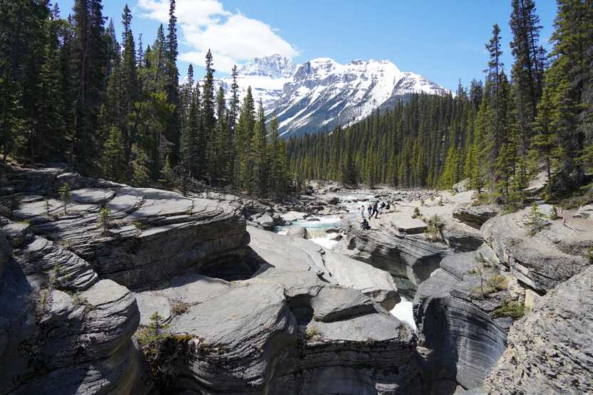 Gray rocks that have been carved away by water to create smooth, swirled rocks. There is a mountain in the background.