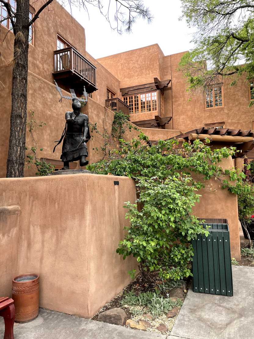 The Pueblo exterior of Hotel Santa Fe. There is a statue mixed in with the landscaping.