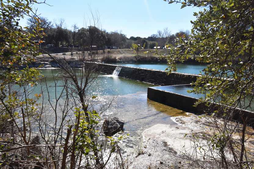 The swimming area of Blanco State Park, which has a dam with a small waterfall flowing over it.