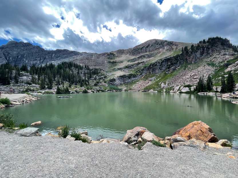 A green colored lake with a rolling mountain top behind it.