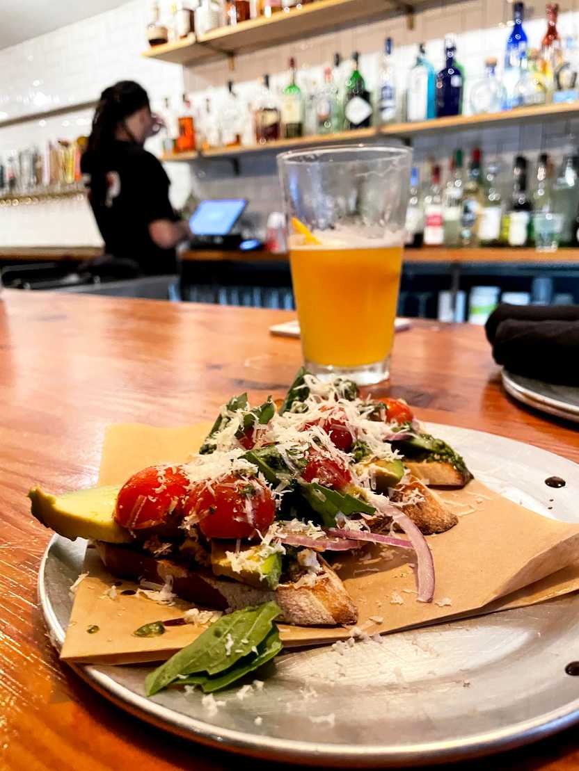 A plate of bruschetta with a beer behind it at the bar at Community Pizza and Beer Garden. A plate of bruschetta with a beer behind it at the bar at Community Pizza and Beer Garden.