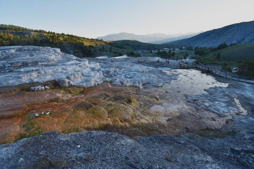 A view of orange and white hardened rock at the Mammoth Hot Springs. There are mountains in the distance.