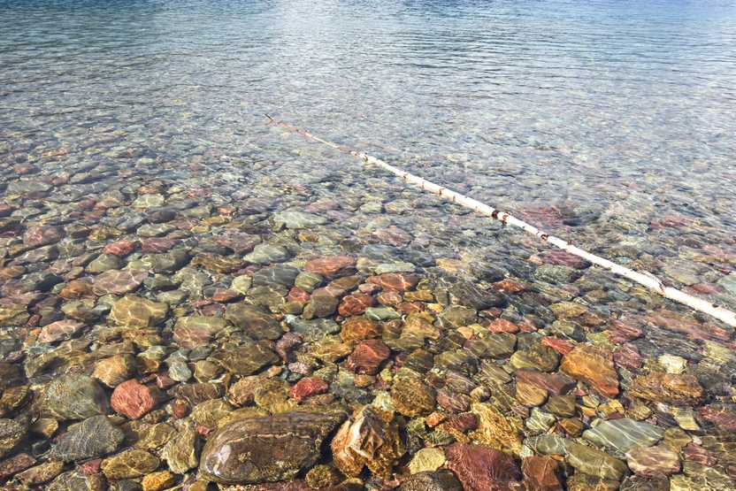 A close up of colorful rocks below the water of Lake McDonald. The rocks are red, yellow and green.