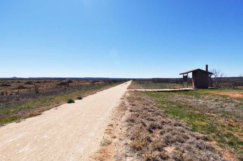 A wide, unpaved trail with a restroom off to the side.