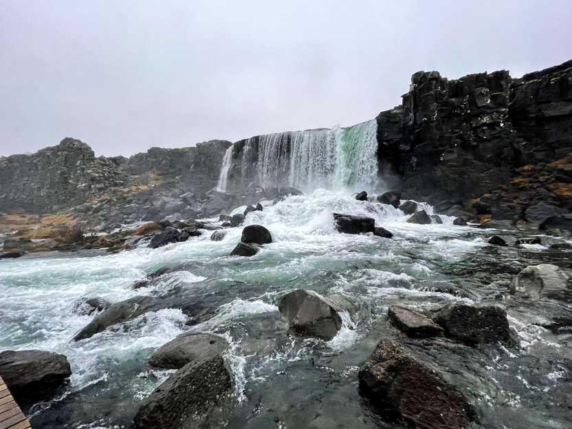 A wide waterfall cascading down a cliff of black rocks.