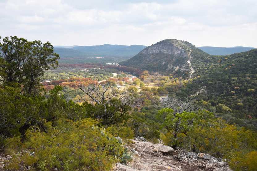 A view of Mt Baldy in Garner State Park. The mountain is covered in green trees and there are red trees in the valley lining the river.