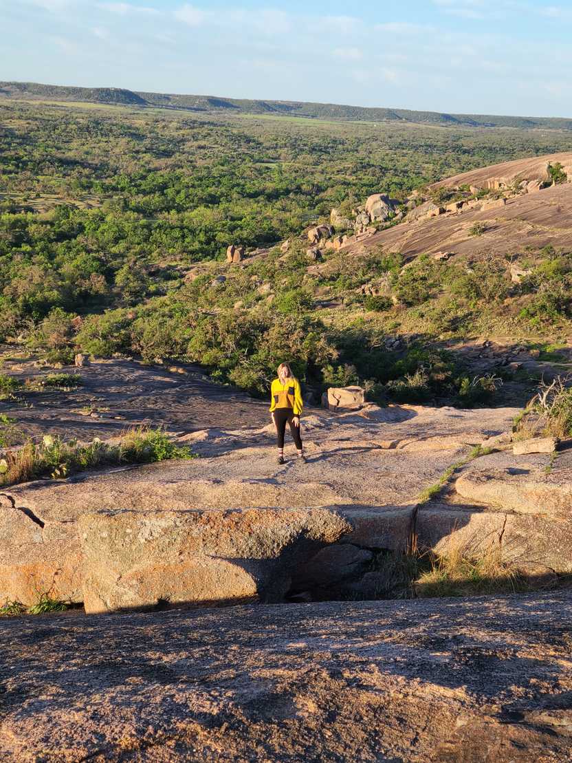 Lydia standing in the distance on enchanted rocks with a view of Hill Country behind her.
