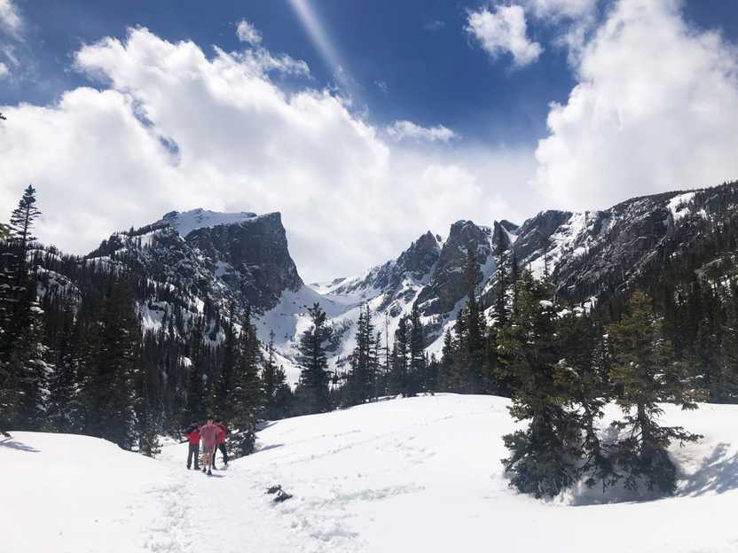 A trail completely covered in snow with mountain peaks in the background.