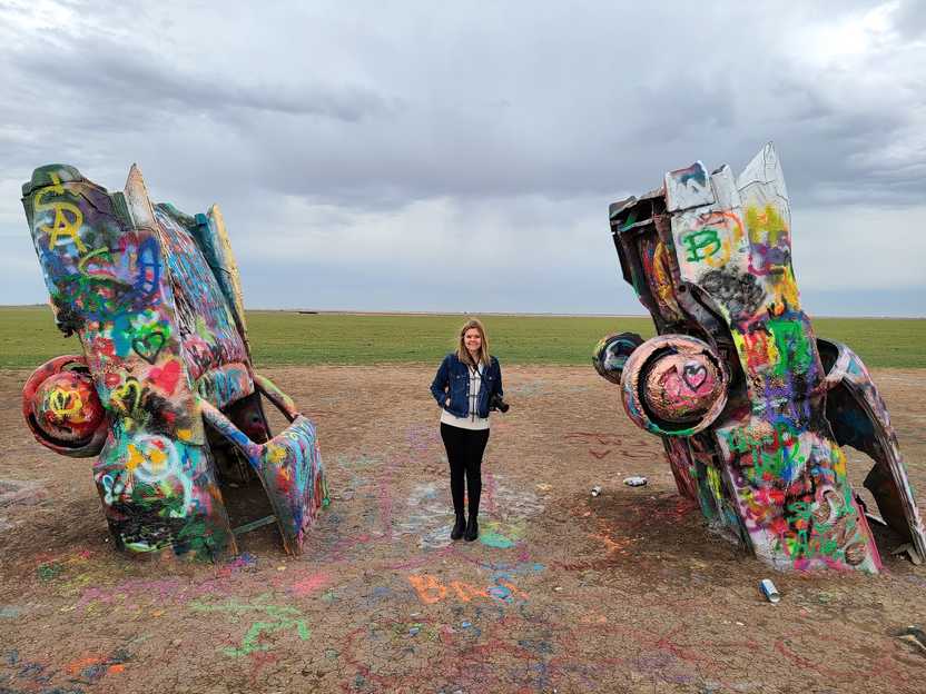 Lydia standing in between two painted Cadillacs.