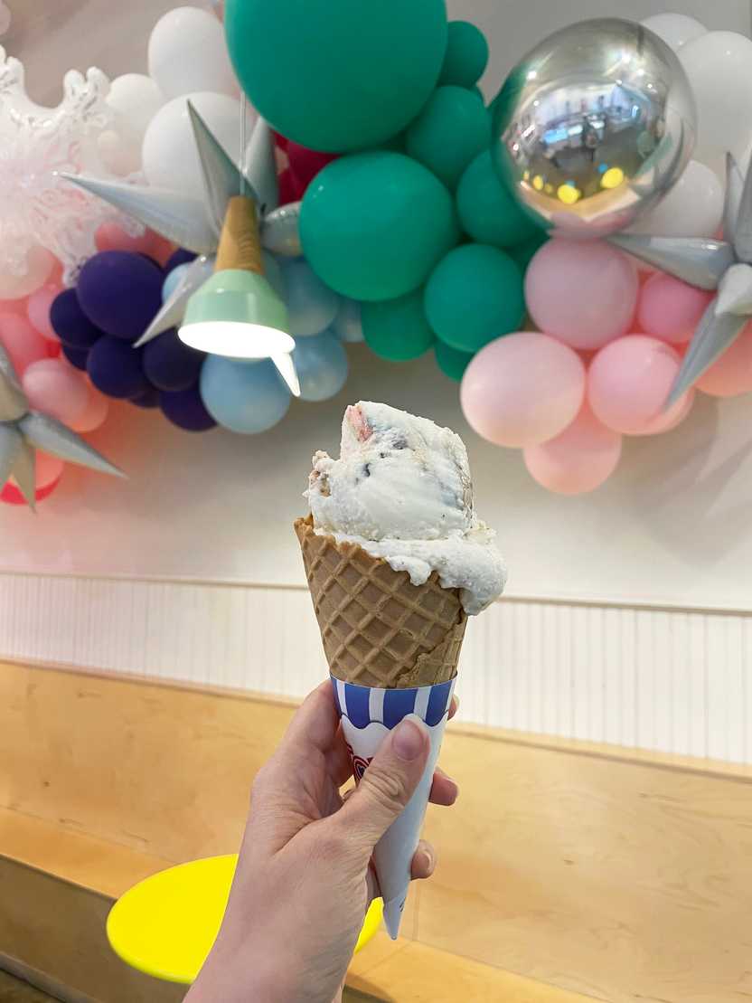 Holding up an ice cream cone in front of some colorful balloons in Loblolly.