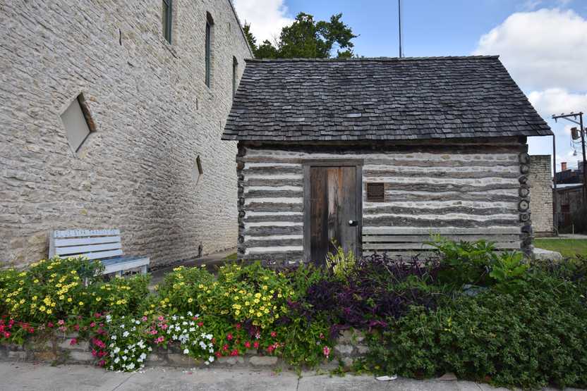 A small log cabin with a bed of flowers in front of it.