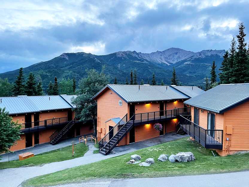 3 buildings part of the Denali Bluffs Hotel with mountains in the distance.