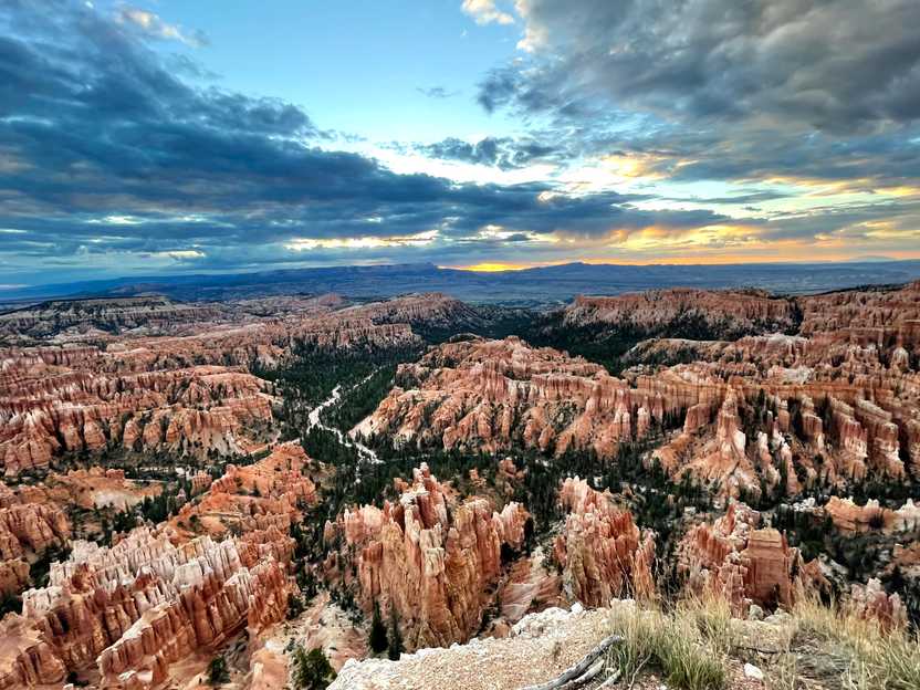 A wide view of many hoodoos from Inspiration Point. It is sunrise and the sky is yellow and orange. You can see a trail through the hoodoos.