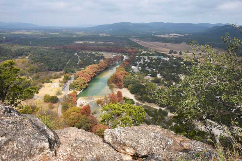 Looking down at the Garner River, which is framed by red trees in the fall. There is an expansive valley beyond the river.