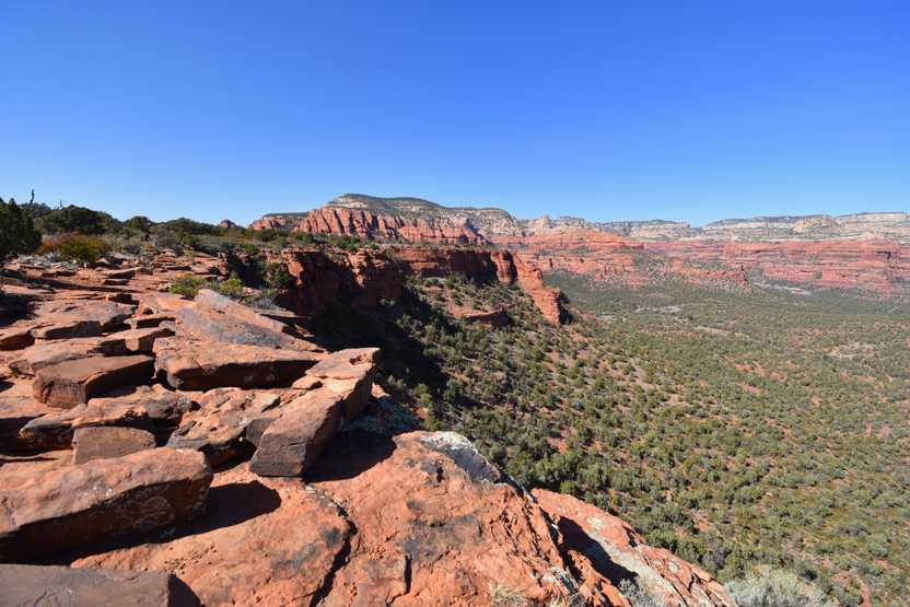 A flat top mountain with views of a valley down below. There are orange and white mountains in the distance.