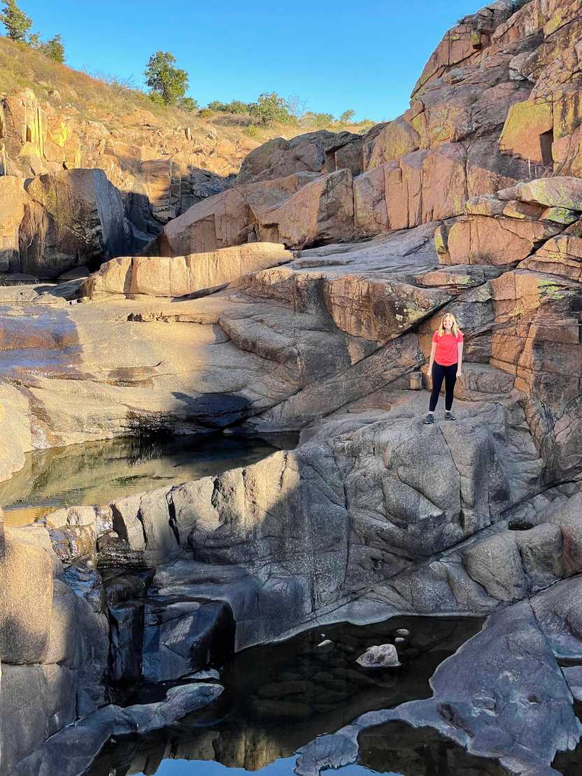 Lydia standing on rocks in the Forty Foot Hole trail. There are some pools of water in the rocks.