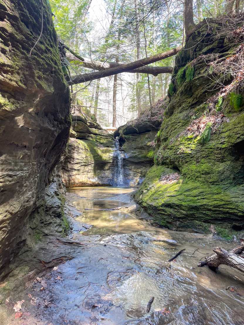 A rocky cove with green moss and a waterfall inside of Turkey Run State Park.