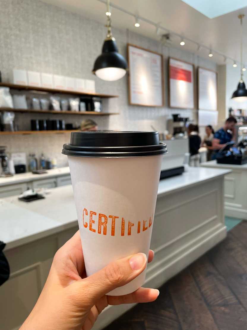 Holding up a to-go coffee mug from Certified Kitchen and Bakery.