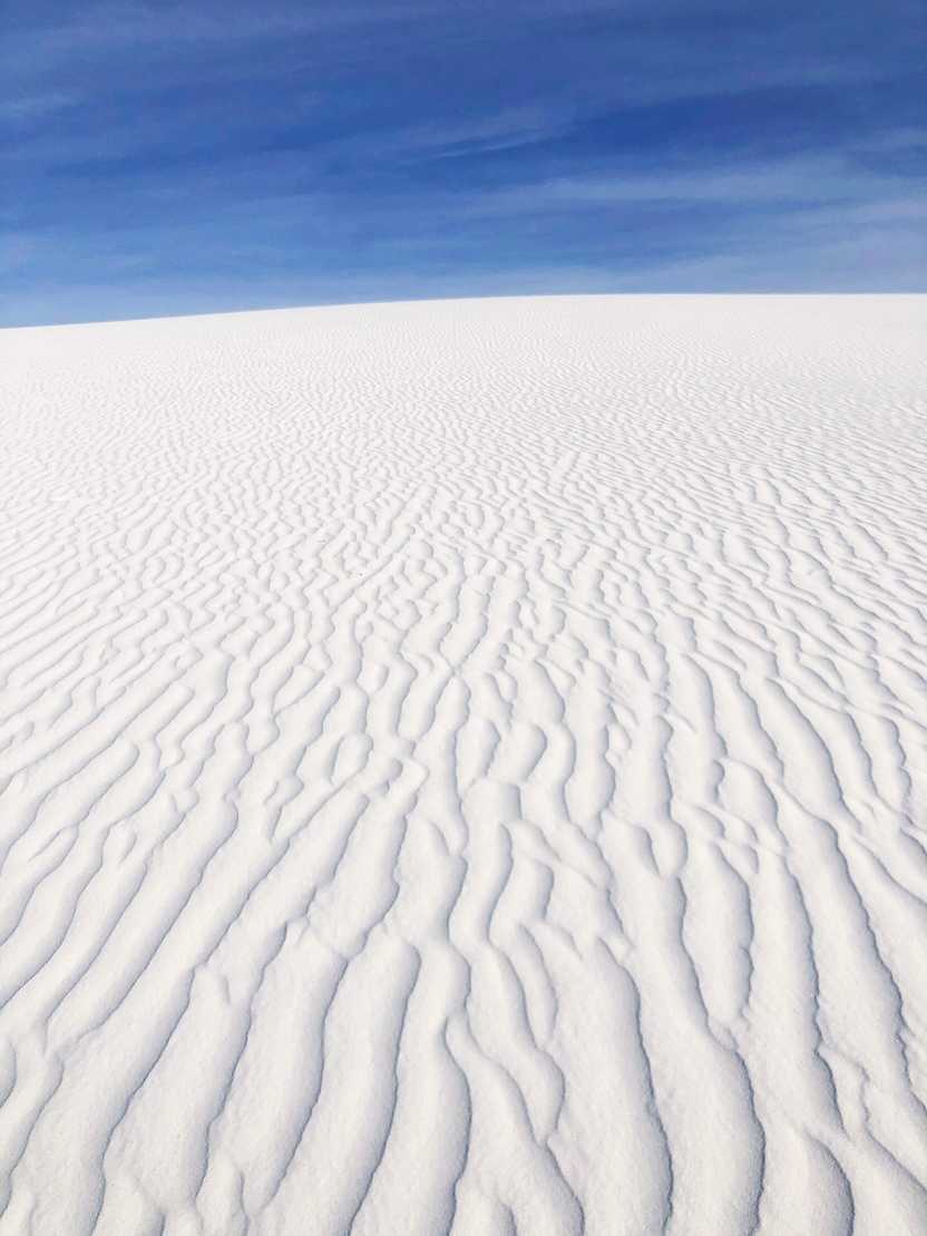 Looking up at a sand dune hill. The wind has created a curved pattern in the sand.