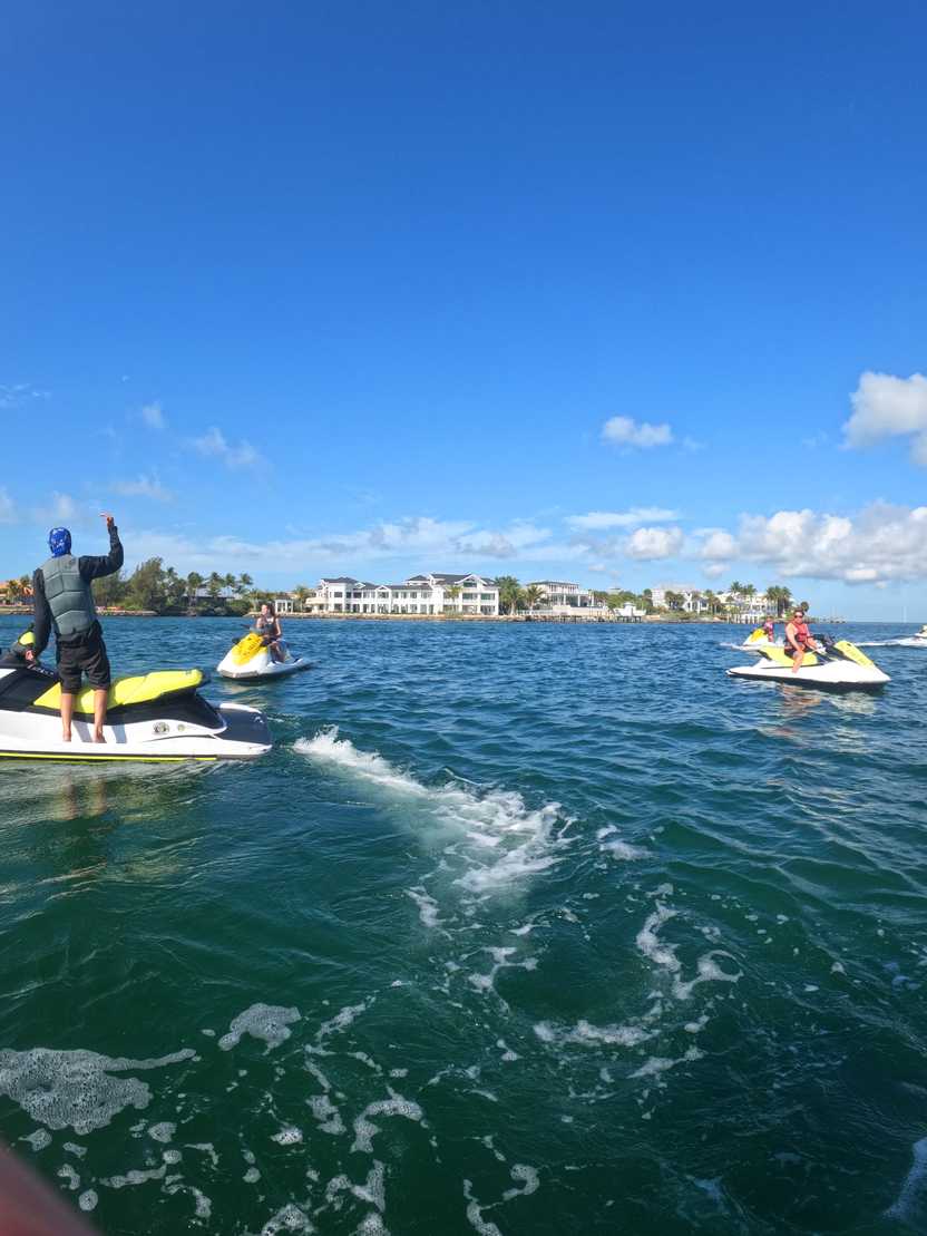 Three jetskis in the water with some large mansions on the shore in the background