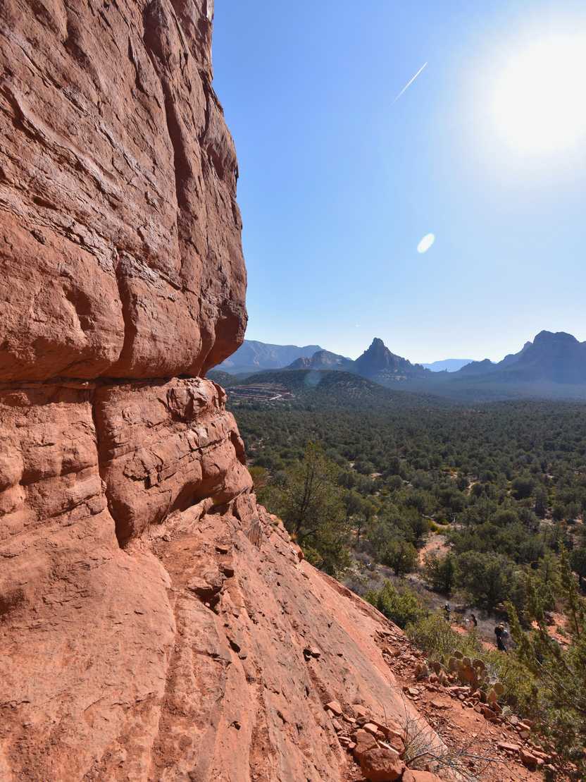 Looking at the side of Birthing Cave. The cave is a curved orange, rock face and there is a view of green trees and some mountains in the distance.