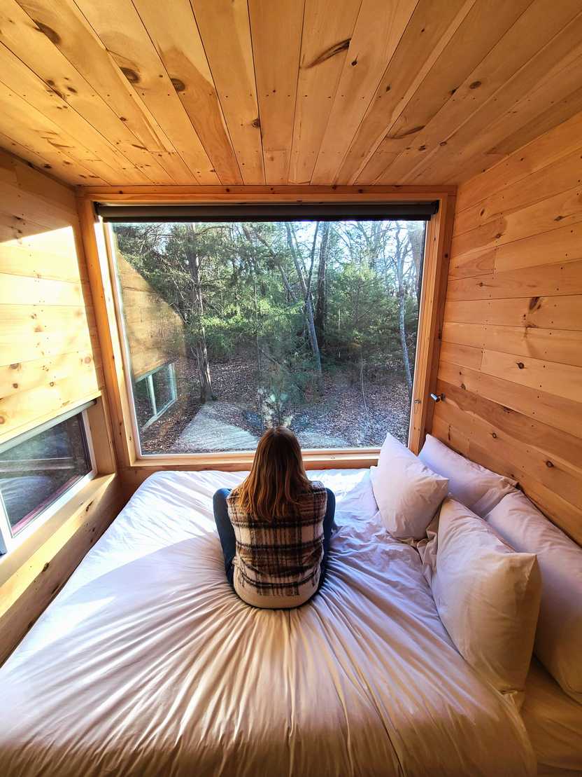 Lydia sitting on the bed and looking out the window inside of the Getaway House.