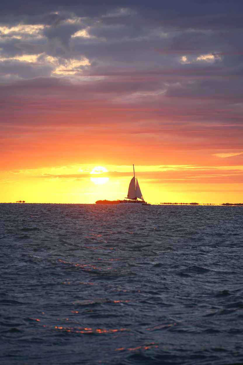 The sunset over the ocean with a sailboat silhouetting the sky