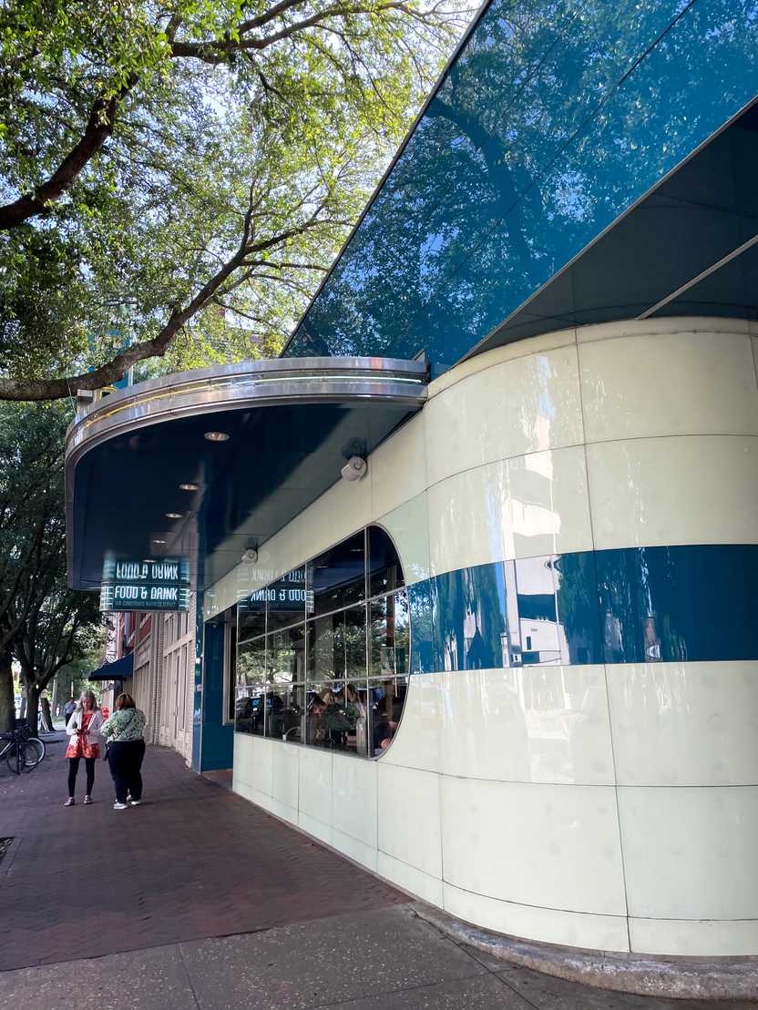 The exterior of the Grey. There are large blue and white stripes. The fancy restaurant is a former Greyhound bus station