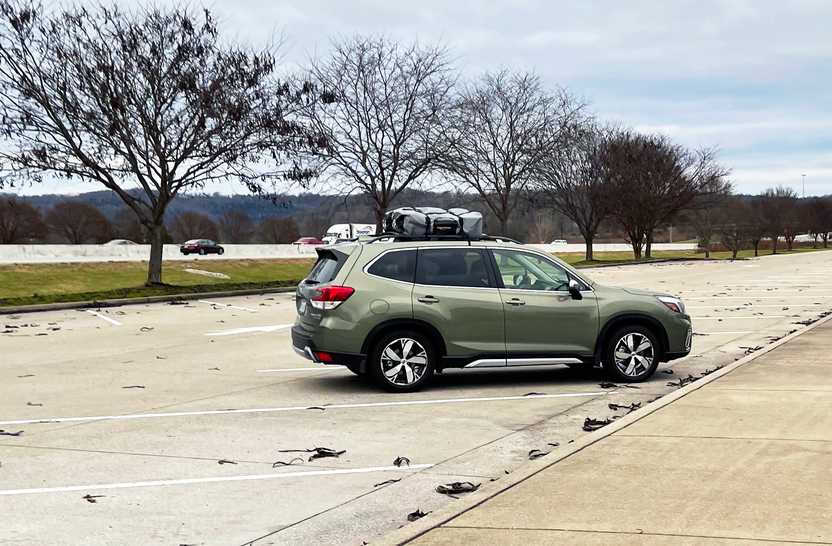 A green Suburu Forester with large duffel bags on the roof.
