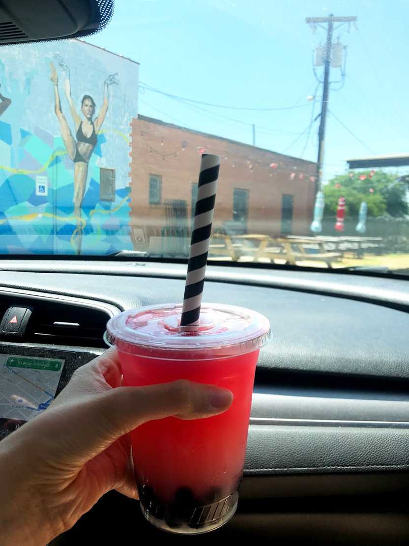 Holding up a plastic cup of dark, pink lemonade from Sandwich Hag