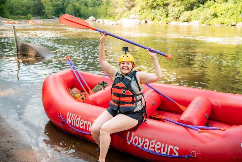 Lydia sitting on the edge of a raft and holding up a paddle before the whitewater rafting trip.