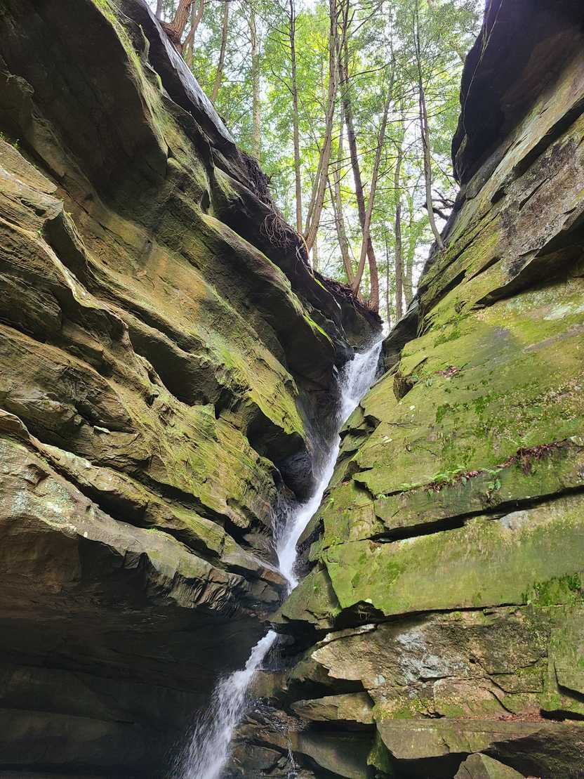 A thin waterfall between two large rocks covered in green moss.