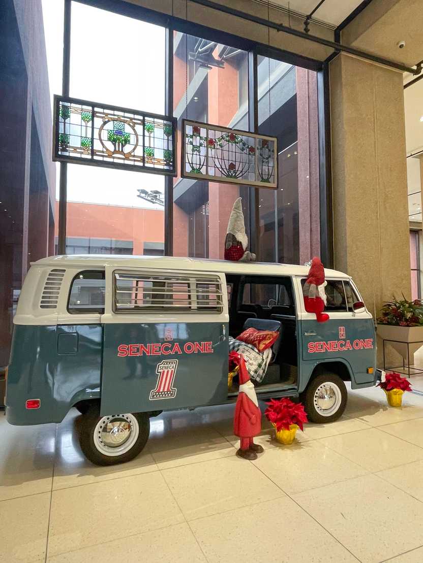 A two toned van that is blue on the bottom and white on the top that reads 'Seneca One.' There is Christmas decor inside and around the van, including small Santa Clause statues.