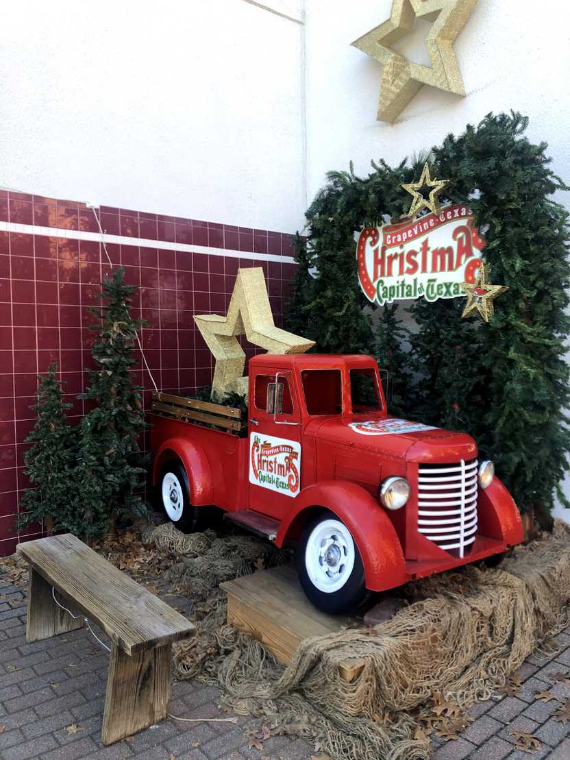 A mini red pick up truck with a gold star in the truck bed. It sits on a bail of hay in front of a background made of green pines. A mini red pick up truck with a gold star in the truck bed. It sits on a bail of hay in front of a background made of green pines.