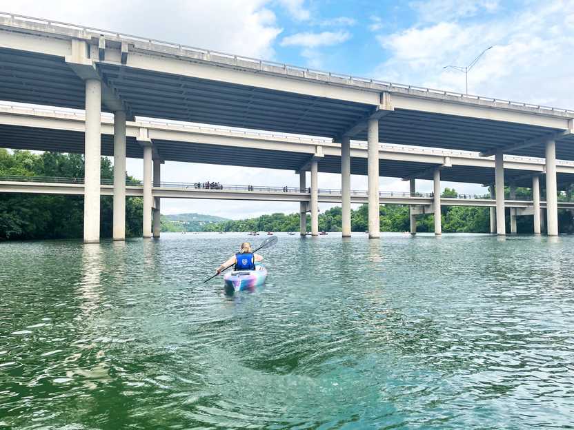 Lydia kayaking under a large bridge in Lady Bird Lake.