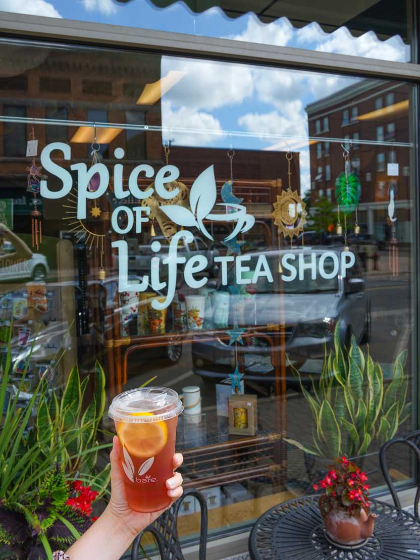 A hand holding a cup of tea in front of Spice of Life Tea Shop A hand holding a cup of tea in front of Spice of Life Tea Shop