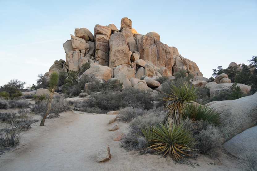 A trail leading up to an interesting piles of various boulders. A few green plants are on the edge of the trail.
